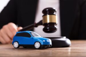 A tiny blue car stands before a judge, who holds a gavel in hand. 