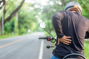 A motorcycle rider touching his lower back and feeling tired after a long motorcycle ride.