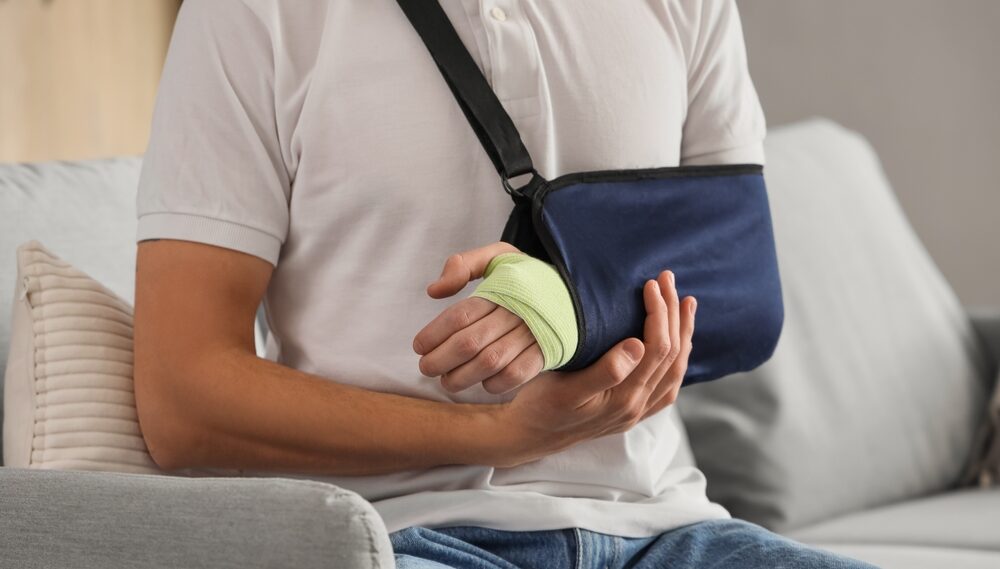 Injured young man after accident sitting on sofa at home, closeup