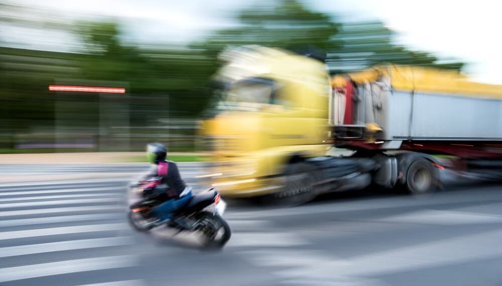 Motocicleta y camión en cruce peatonal, escena borrosa que sugiere un accidente vial.