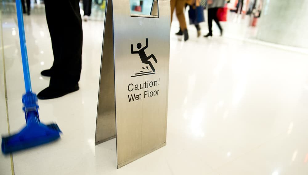 Wet floor sign next to cleaning in progress in a busy shopping center.