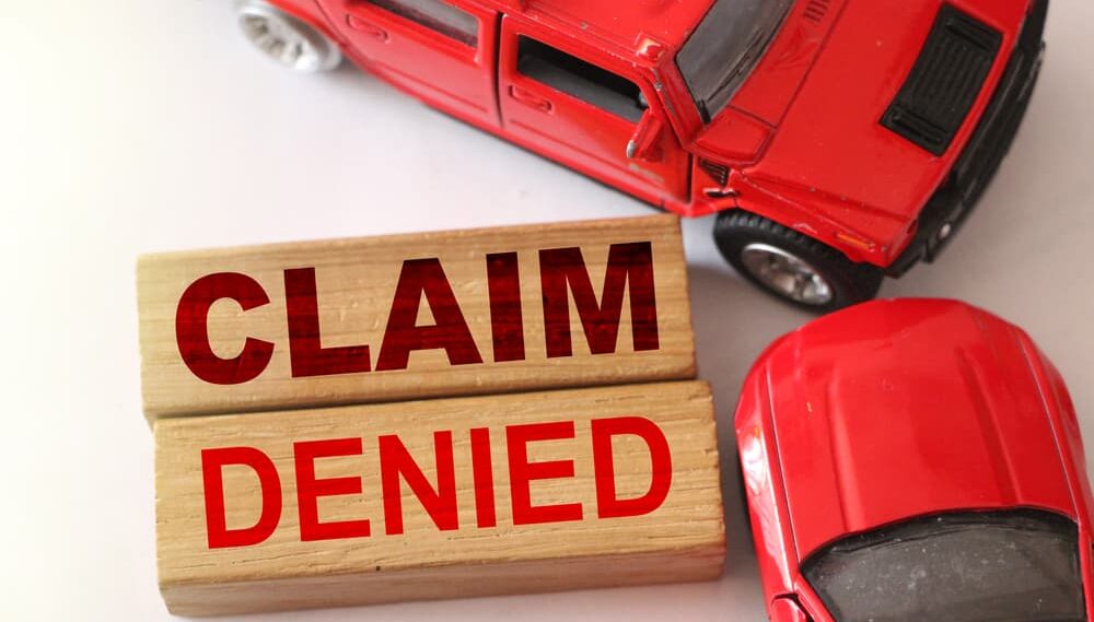 Claim denied words on wooden blocks and two red cars in road accident on white.