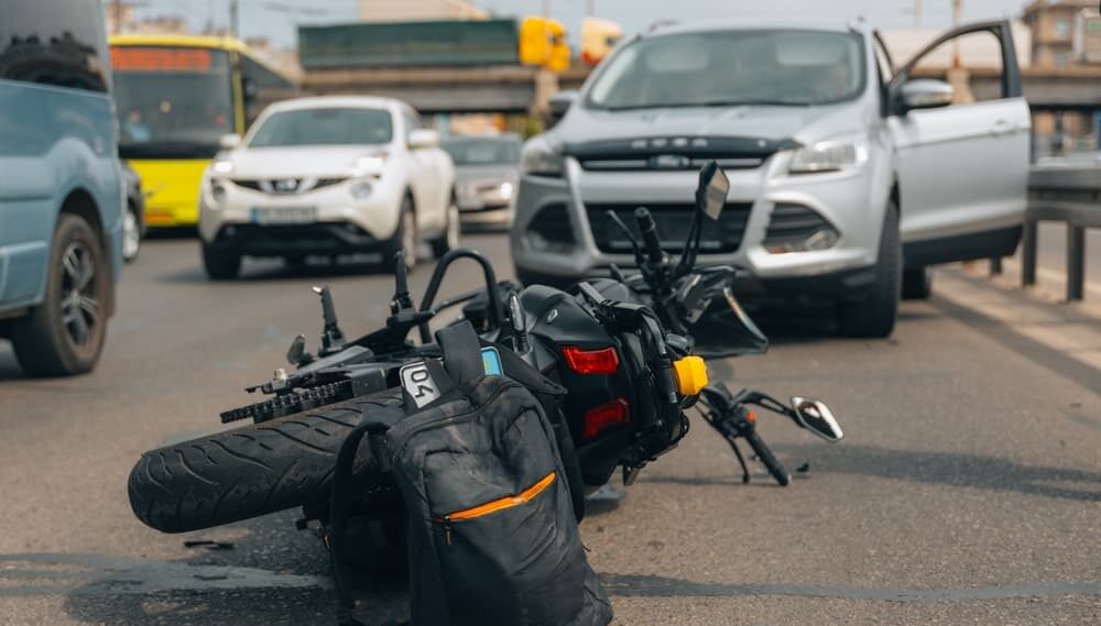 Motorcycle accident on a busy road, with a car involved, possibly due to poor signage.